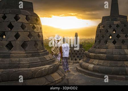 Vue d'une femme et d'un enfant silhouettés contre le coucher de soleil ardent entre les anciens stupas, Temple Borobudur, Magelang, Java central, Indonésie. Banque D'Images
