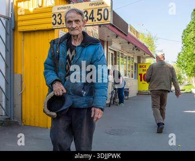 Kiev, Ukraine - 12 mai 2022 : homme âgé en veste bleue tenant un chapeau sur le trottoir de Kiev près d'un signe de change, portrait de la détresse urbaine et Banque D'Images