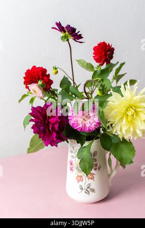 Un vase contient une variété de fleurs fraîches avec différentes couleurs. Les fleurs sont placées sur une table rose. Derrière le vase se trouve un mur Uni dans un roo lumineux Banque D'Images