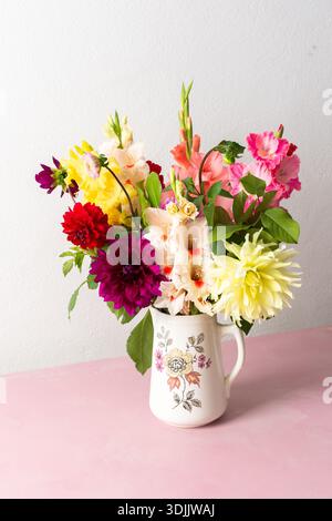 Un vase contient une variété de fleurs fraîches avec différentes couleurs. Les fleurs sont placées sur une table rose. Derrière le vase se trouve un mur Uni dans un roo lumineux Banque D'Images
