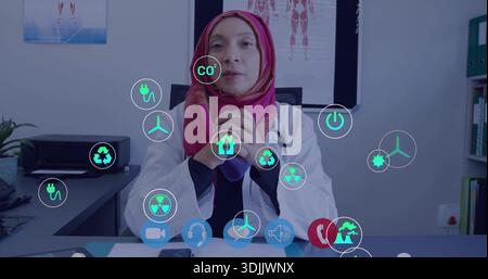Médecin assis portant une blouse de laboratoire blanche hijab rose au bureau de la clinique, montrant stéthoscope, icônes d'énergie Banque D'Images