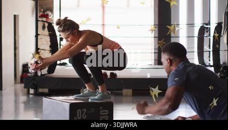 Femme performante tenant squat sur la boîte plyo dans la salle de gym près de l'anneau de boxe, portant débardeur pêche Banque D'Images