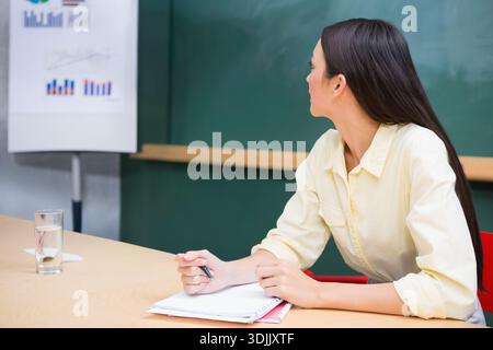 Cahier en spirale et stylo reposent sur une table en bois dans la salle de classe avec tableau à feuilles mobiles, verre d'eau. Tableau noir, graphiques, présentation, apprentissage, formation, à Banque D'Images