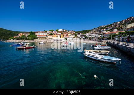 Petits bateaux dans le port de Rabac avec hôtels en bord de mer et bâtiments résidentiels. Les collines boisées sont visibles au loin. Banque D'Images