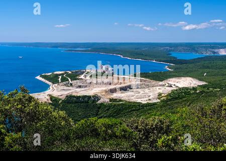 Vue sur une carrière de calcaire et une cimenterie sur la côte de Koromačno. La mer Adriatique et les collines boisées sont visibles au loin. Banque D'Images