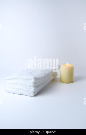 Spa minimal Still Life : serviettes blanches pliées et une petite bougie allumée sur un fond doux et lumineux avec espace de copie. Banque D'Images