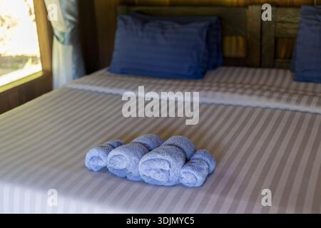 Lit accueillant de la chambre d'hôtel avec des serviettes propres et roulées et oreiller bleu. Cette scène relaxante met en valeur l'hospitalité et le service pour un hébergement confortable Banque D'Images