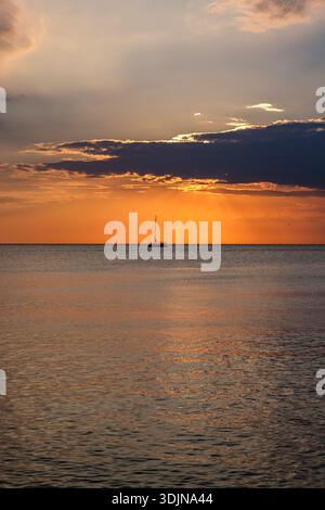Coucher de soleil sur la mer à Porec. Un voilier solitaire est visible sur l'eau calme contre un ciel orange brillant avec des nuages sombres. Banque D'Images