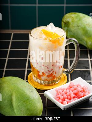 Une boisson vibrante et rafraîchissante à la mangue sucrée servie dans une tasse en verre transparent, avec des morceaux de mangue mûre, un liquide crémeux et de minuscules perles de sagou rose. FR Banque D'Images