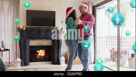 Couple mature dansant se tenant la main dans le salon, portant des chapeaux de Père Noël, manteau et icônes AR sarcelle. Cheminée, noël, confortable, festif, intérieur, garla Banque D'Images