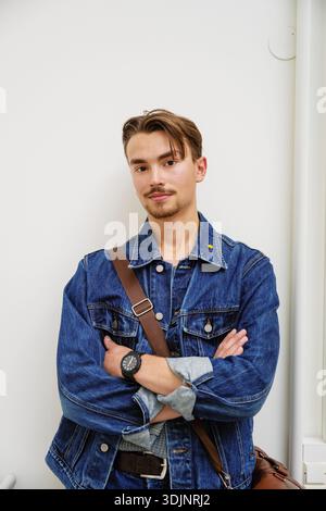 Portrait d'un jeune homme confiant debout avec les bras croisés près du mur à l'université Banque D'Images