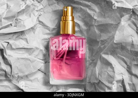 Bouteille de pulvérisation de parfum en verre rose sur fond de papier artisanal froissé blanc Banque D'Images
