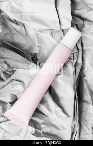 Tube de produit de beauté rose vierge reposant sur un fond de papier d'emballage froissé Banque D'Images