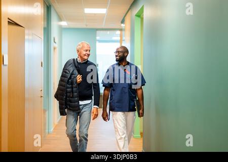 Infirmier souriant marchant avec un homme âgé dans le couloir de l'hôpital Banque D'Images