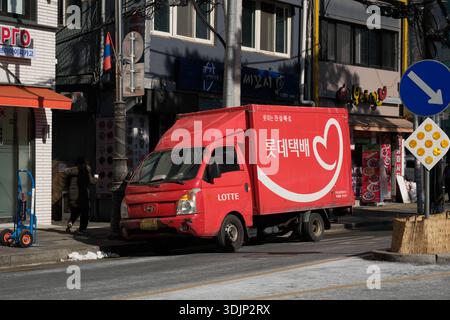 Séoul, Corée du Sud : camion de livraison de courrier Red Lotte conduisant dans une rue commerçante étroite avec des magasins et des restaurants Banque D'Images