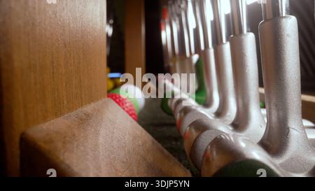 Gros plan de mini-putters de golf de différentes tailles et couleurs organisés dans un rack en bois, avec des balles de golf colorées prêtes pour le jeu Banque D'Images