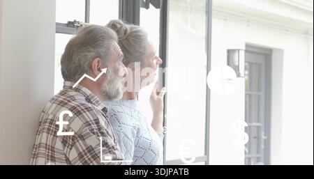 Couple senior debout en pull bleu, chemise à carreaux regardant par la fenêtre à la maison, superpositions financières Banque D'Images