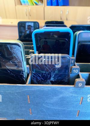 Collection de smartphones avec des écrans fissurés disposés dans un organisateur en bois sur une table, mettant en évidence différentes couleurs et modèles dans un cadre de réparation Banque D'Images