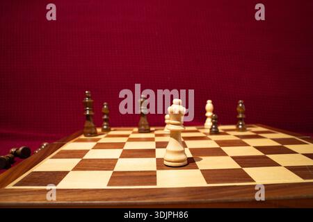 Pièce de roi blanche sur un échiquier en bois avec d'autres pièces floues en arrière-plan. Gros plan d'une partie en cours. Concept de stratégie, échecs, Banque D'Images