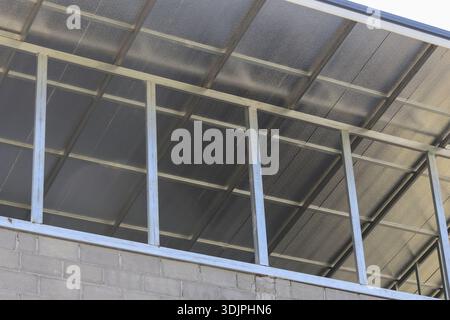 Gros plan sur la structure robuste d'un auvent en métal avec la tôle de toit translucide fixée au mur de béton gris montrant les détails de construction extérieure durable pour la résolution Banque D'Images