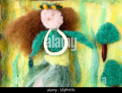 Figure en laine d'une femme aux cheveux bruns et robe verte dans un paysage vibrant avec des arbres et des formes abstraites faites de fibres de laine feutrées Banque D'Images