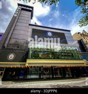 Vue extérieure du cinéma Odéon sur Leicester Square à Londres, montrant la façade de verre moderne, la tour et l'écran numérique promouvant des films sous un bri Banque D'Images