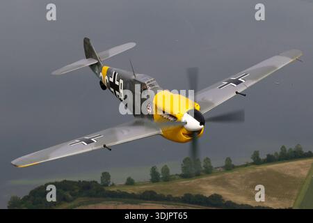 La photographie représente l'Hispano HA‑1112‑M1L Buchón, une version espagnole de la cellule Bf‑109 d'après‑seconde Guerre mondiale propulsée par un moteur à pistons Rolls‑Royce Merlin 500‑45 V‑12 avec une hélice à quatre pales, portant l'enregistrement civil G‑AWHH aux couleurs de l'armée de l'air allemande avec le code militaire 9 et le numéro de série 145 chez UK Warbirds 2019. L’image met l’accent sur la zone du poste de pilotage avec la vue du pilote et les surfaces aérodynamiques du chasseur monoplace. La prise de menton distinctive de Buchón, la centrale électrique Merlin, la disposition des ailes basses et le schéma de peinture historique sont visibles lorsqu’elle vole en formation au niveau de la disp 1112 Banque D'Images