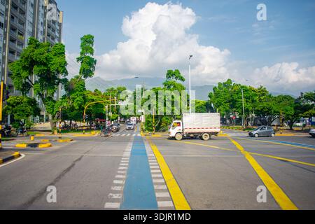 Une scène urbaine vibrante montrant une intersection à Cali, Valle del Cauca, avec des arbres verts et des véhicules en mouvement sous un ciel bleu clair. Banque D'Images