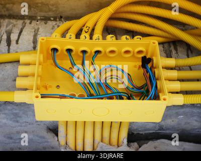 L'image montre une boîte de jonction en plastique jaune montée sur un mur en béton, avec plusieurs conduits ondulés jaunes connectés à elle. Banque D'Images