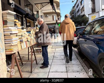 Stalle de livres usagée avec des piles de littérature d'occasion sur un trottoir de la ville. Client plus âgé parcourant des livres sur un marché de livre en plein air à Athènes, Grèce. Banque D'Images
