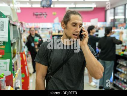 Jeune homme parlant au téléphone dans l'allée du supermarché Banque D'Images