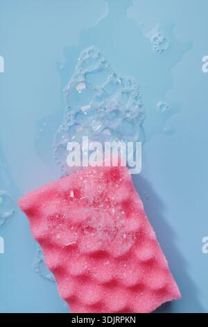 Éponge en mousse rose sur fond bleu avec des bulles de liquide et de savon Banque D'Images