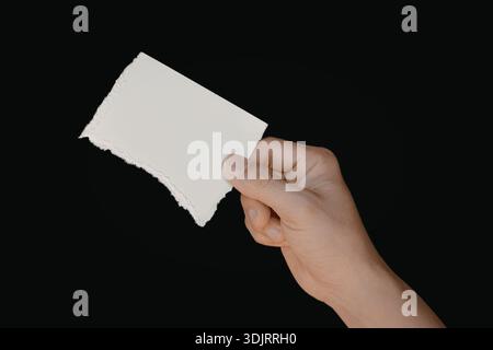 Gros plan d'une main tenant un seul morceau de papier blanc sur un fond noir. Banque D'Images