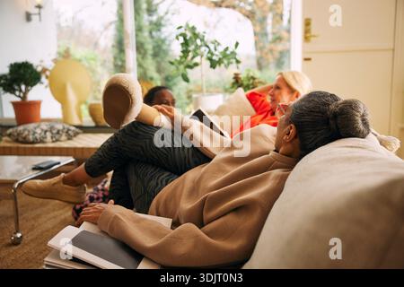 Femme mature confortablement appuyée sur le canapé tout en profitant du temps libre avec des amis à la maison Banque D'Images