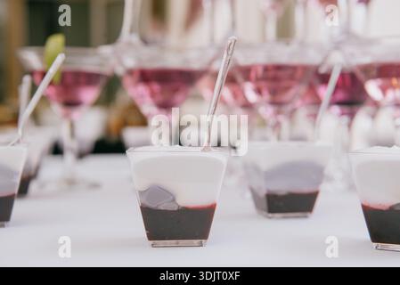 Desserts aux myrtilles en couches dans des tasses transparentes avec cuillères en plastique. Bonbons en mousse en portions avec baies noires et crème blanche pour les vacanciers Banque D'Images