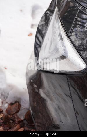 Phare de voiture noir, vue rapprochée, image de voiture recadrée. Voiture garée. Phare et neige. Voyage hivernal en voiture. Banque D'Images