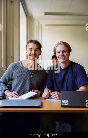 Portrait de jeunes étudiants masculins souriants assis à un bureau dans une salle de classe universitaire Banque D'Images