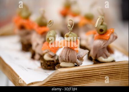 Hors-d'œuvre de viande assortis sur du pain noir et desserts sur une table servie. Mini-hors-d'œuvre de restauration exquis sur des plateaux dans une salle d'événement lumineuse Banque D'Images