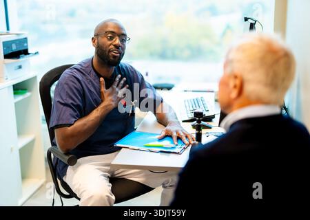 Professionnel médical masculin parlant avec un homme âgé tout en étant assis au bureau à l'hôpital Banque D'Images