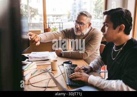 Homme d'affaires mature aidant collègue masculin travaillant sur ordinateur dans la société de conception Banque D'Images