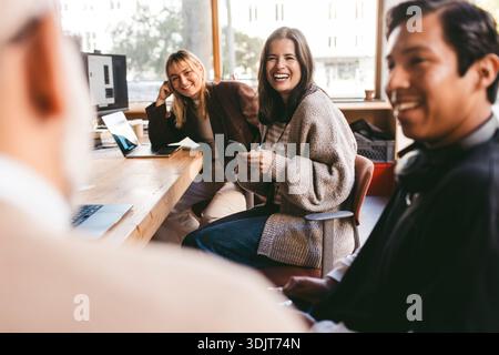 Femme d'affaires heureuse tenant le téléphone intelligent parlant avec un collègue tout en étant assis près du bureau dans le bureau Banque D'Images