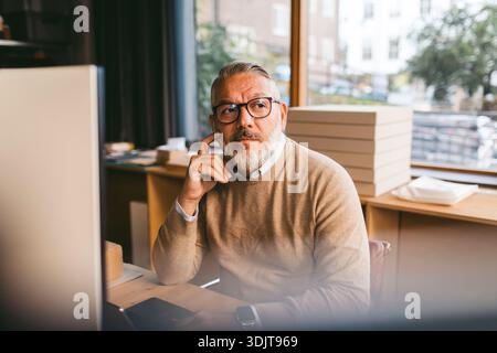 Professionnel mûr réfléchi de conception masculine assis au bureau dans le bureau Banque D'Images