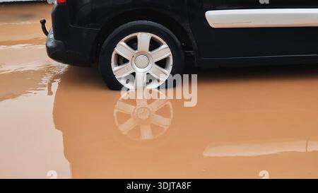 Voiture conduisant dans une rue urbaine inondée éclaboussant de l'eau boueuse sous de fortes pluies Banque D'Images