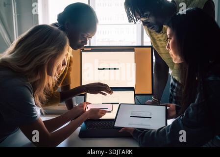 Professionnels créatifs féminins et masculins comparant les appareils tout en travaillant dans un bureau technique Banque D'Images