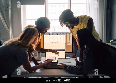 Professionnels créatifs féminins et masculins comparant des logiciels sur différents appareils tout en travaillant dans un bureau technique Banque D'Images