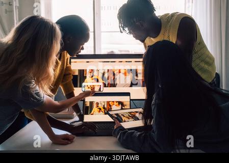 Professionnels créatifs féminins et masculins comparant l'aperçu de conception sur différents appareils tout en travaillant dans un bureau technique Banque D'Images