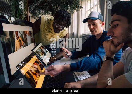 Professionnels de la technologie créative masculine comparant la prévisualisation de conception réactive sur différents appareils au bureau Banque D'Images