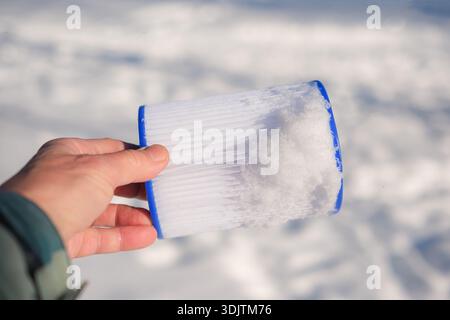 Filtre à cartouche de piscine réutilisable recouvert de neige dans la main humaine. Fond de neige blanche propre. Faible profondeur de champ. Copier l'espace. Banque D'Images