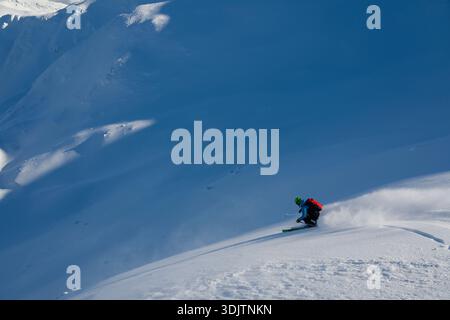 Skieur sculpte dans la poudreuse fraîche sur une pente de montagne bleue dans des conditions hivernales immaculées Banque D'Images