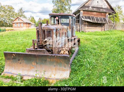 Tracteur rouillé à chenilles abandonné vintage sur l'herbe verte au village dans la journée d'été Banque D'Images